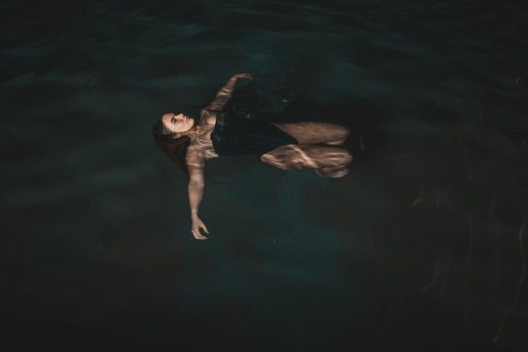 A woman peacefully floats on her back in a dark, serene swimming pool at night, exuding relaxation.